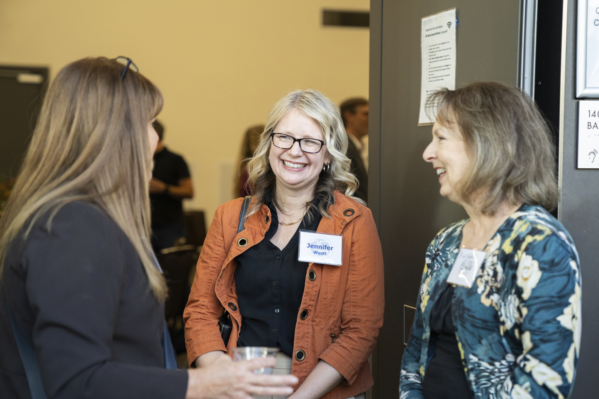 Three women smiling and chatting at a networking event, one holding a drink (photo)