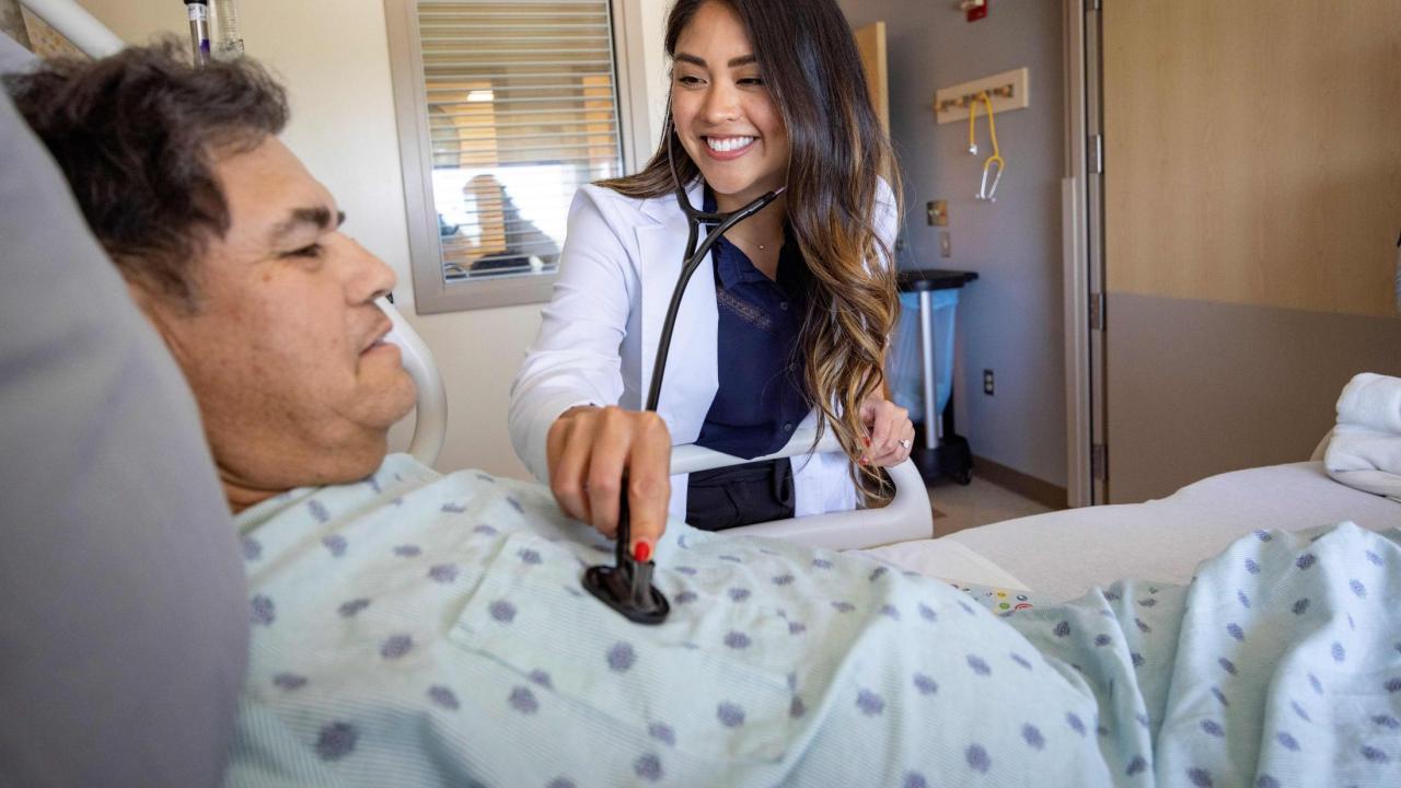 Female doctor has her stethoscope out checking a man's heartbeat. The man is a patient laying in bed.