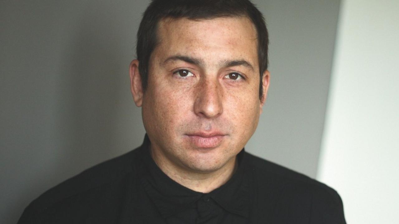 Head-and-shoulders portrait of a man with short dark hair, neutral expression, black shirt