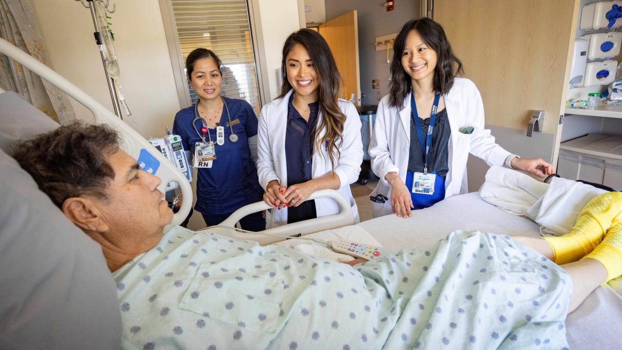 Three female medical staff standing next a male patient's bed.