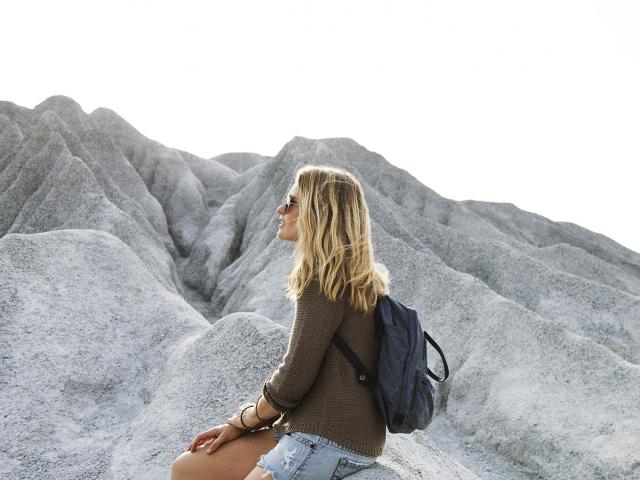 young woman sitting alone on a rock looking into the distance