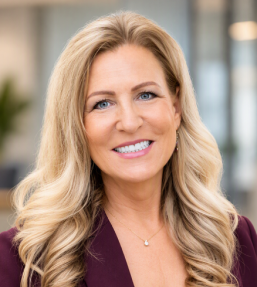 Professional headshot photograph of a smiling middle-aged woman with long wavy blonde hair, maroon blazer