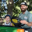 Employee driving tractor with young child beside him